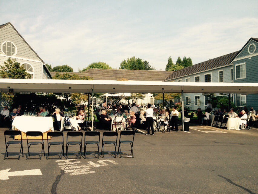 An outdoor gathering with people seated under a large tent on a sunny day.