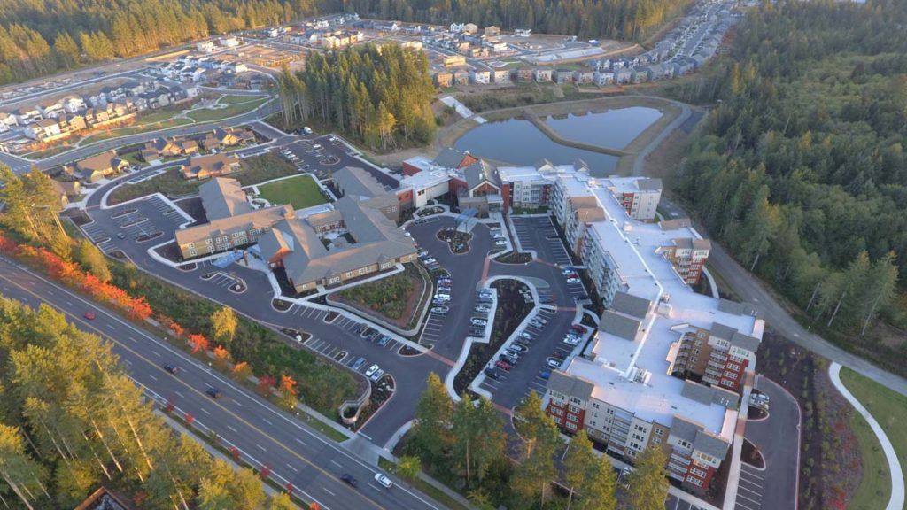 An aerial view of a complex with buildings, parking lots, and surrounding roads and trees in a residential area.