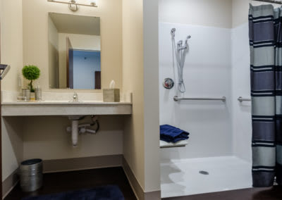 An accessible bathroom featuring a walk-in shower, sink with mirror, and grab bars.