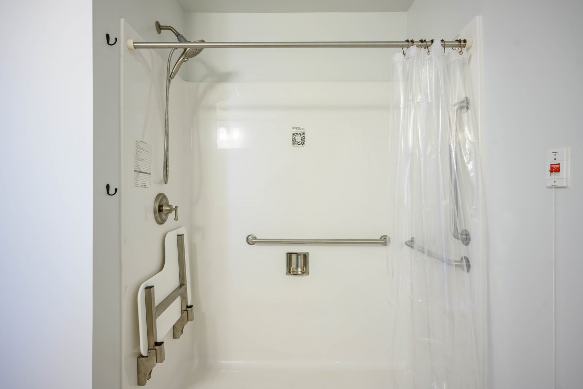 A modern, accessible white shower with grab bars and a shower curtain.