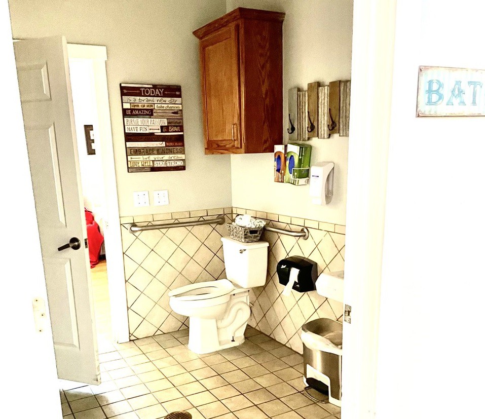 A clean and well-organized bathroom with a tiled floor, featuring a toilet, wall cabinet, and dispensers for soap and toilet paper.