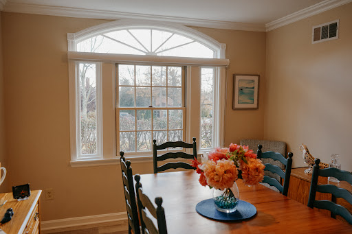 A cozy dining area featuring a wooden table adorned with a vibrant flower arrangement and large windows letting in natural light.