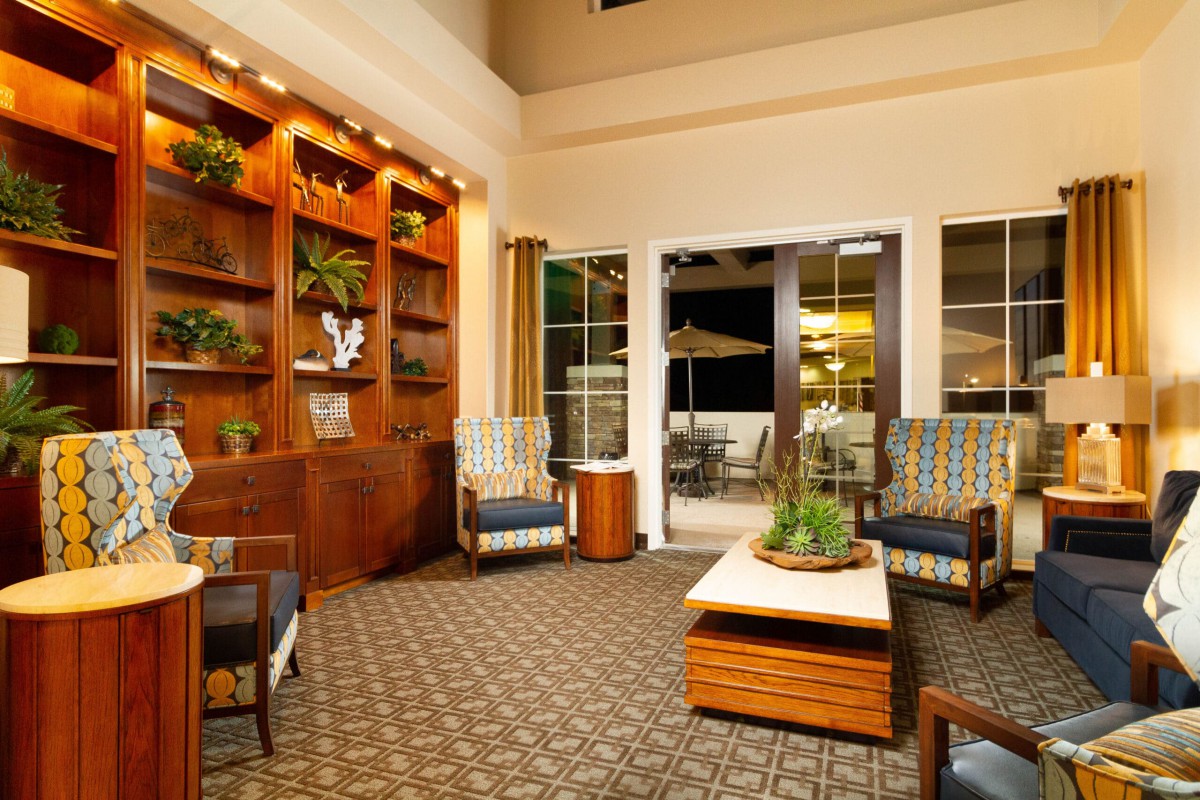 A cozy hotel lobby featuring comfortable seating, a wooden bookshelf, and indoor plants.