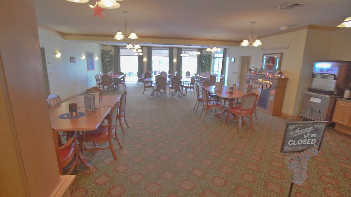 A spacious dining area with multiple tables and chairs, illuminated by chandeliers.