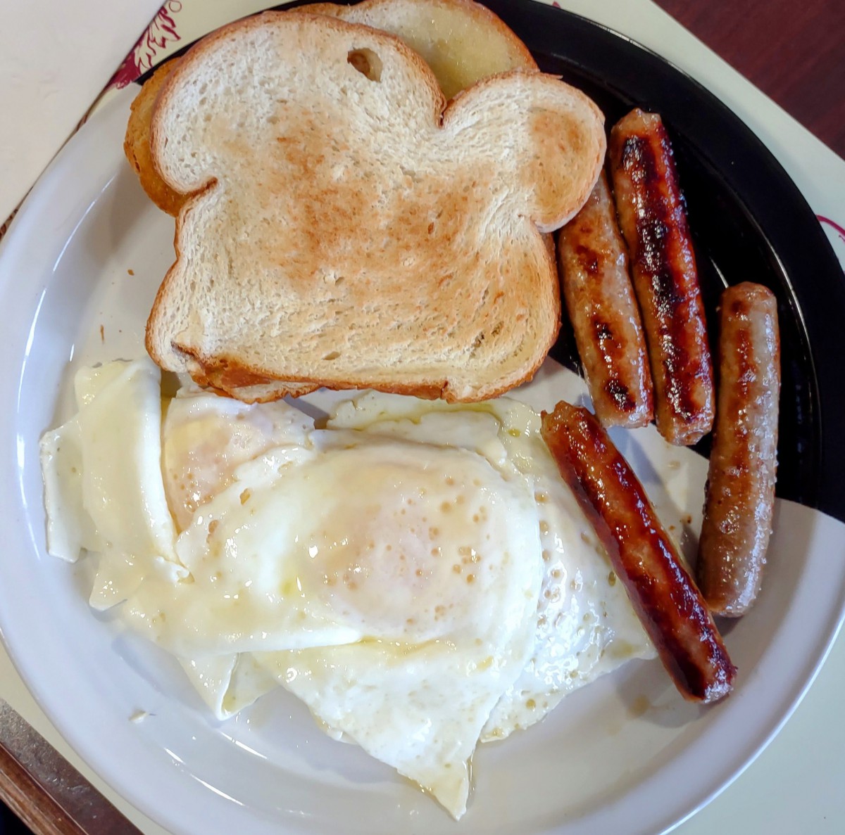 A classic breakfast plate with toast, eggs, and sausages.