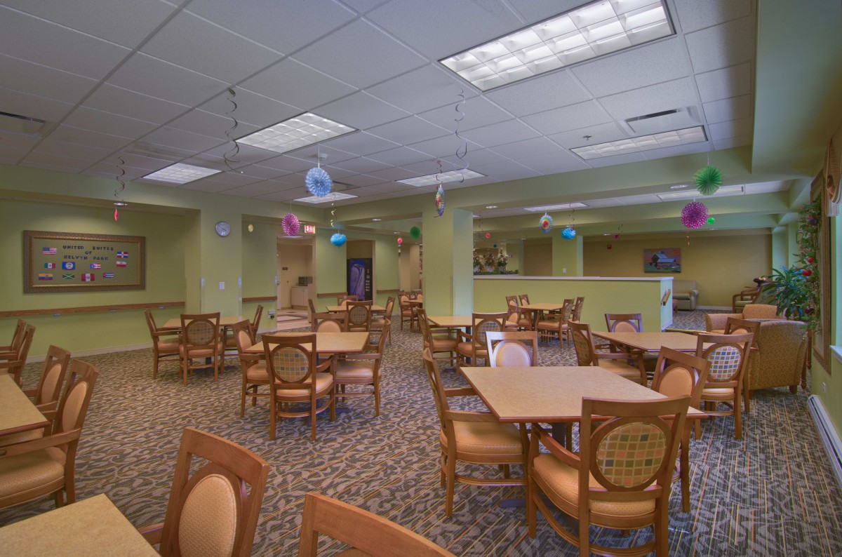 An empty dining area with neatly arranged tables and chairs, featuring a carpeted floor and ceiling lights.