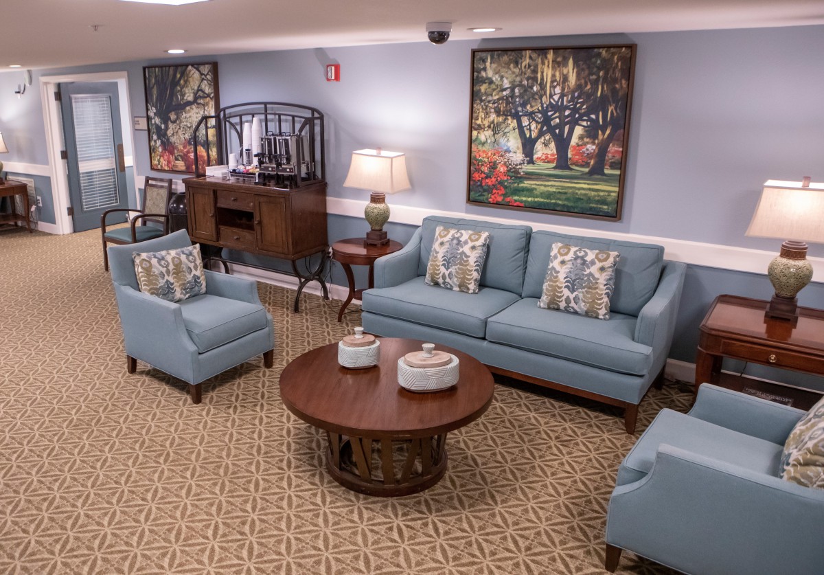 A cozy living room featuring blue sofas and armchairs, a wooden coffee table, and decorative artwork on the walls.