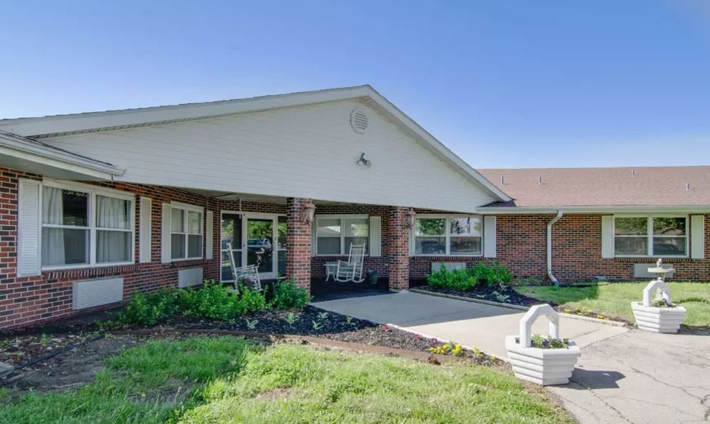 A single-story brick residential building with a landscaped front yard and driveway.