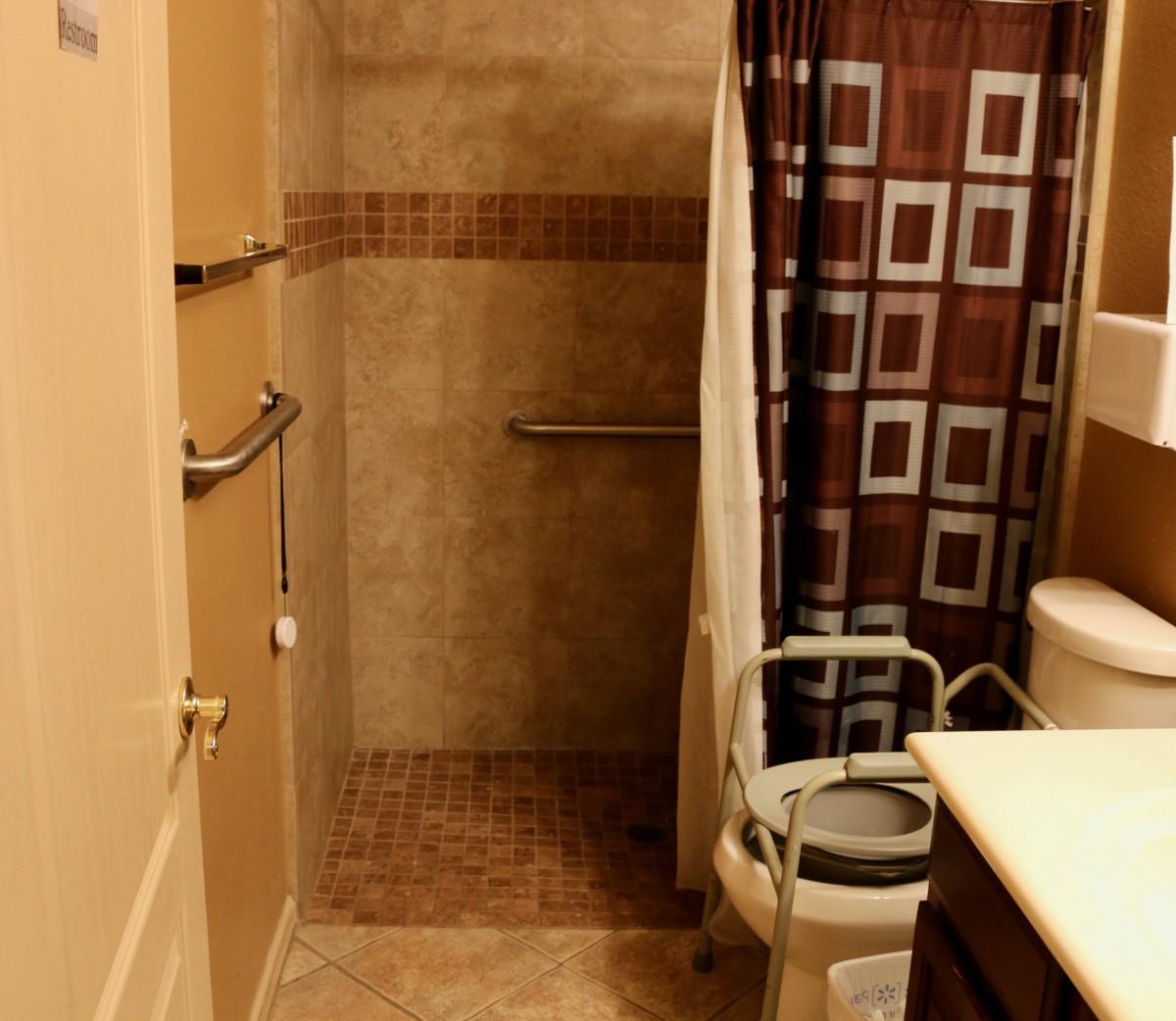An accessible bathroom with a walk-in shower, grab bars, and a patterned shower curtain.