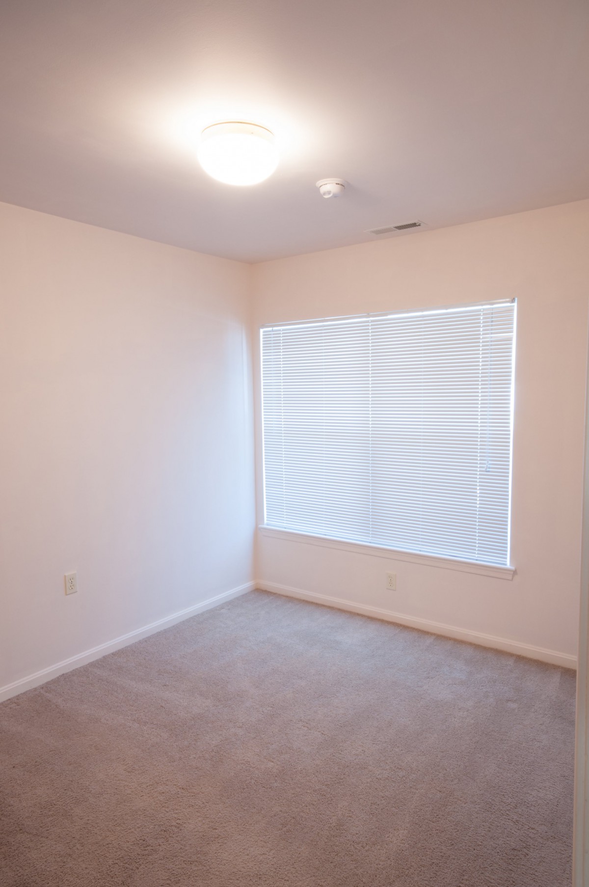 An empty room with carpeted flooring and a large window covered with blinds.