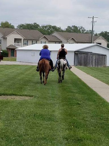Two individuals riding horses through a grassy area in a residential neighborhood.