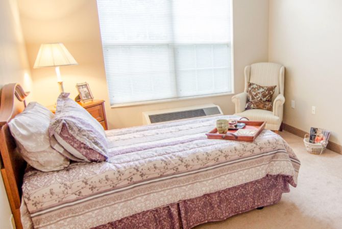 A cozy bedroom with a neatly made bed, armchair, and bedside lamp.