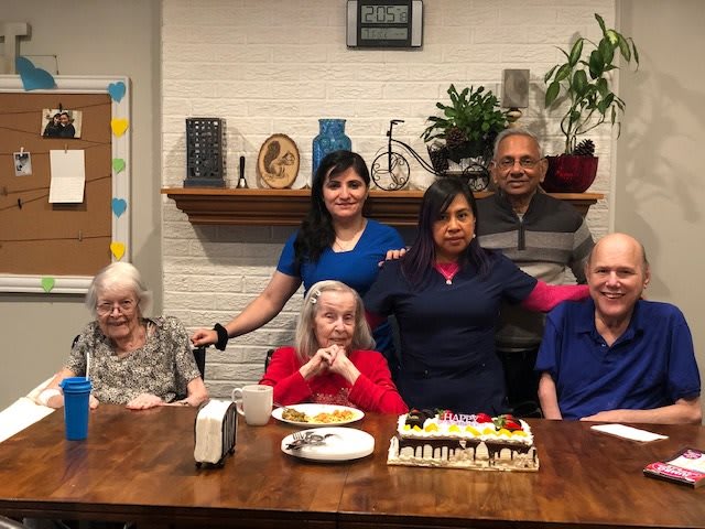 A group photo capturing a celebration with seniors and caregivers gathered around a table with a cake.