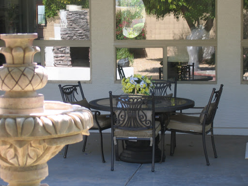A serene outdoor patio setting with a fountain, table, and chairs surrounded by lush greenery.