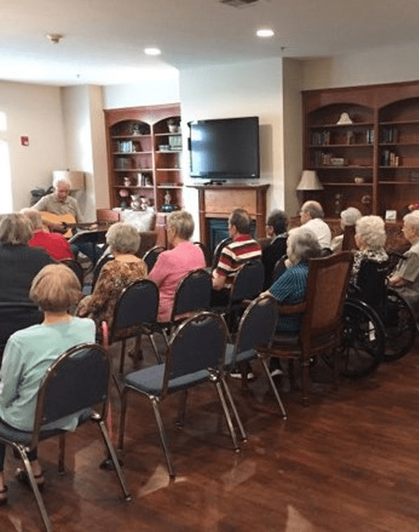 A group of seniors gathered indoors for a community event, seated and attentively listening.