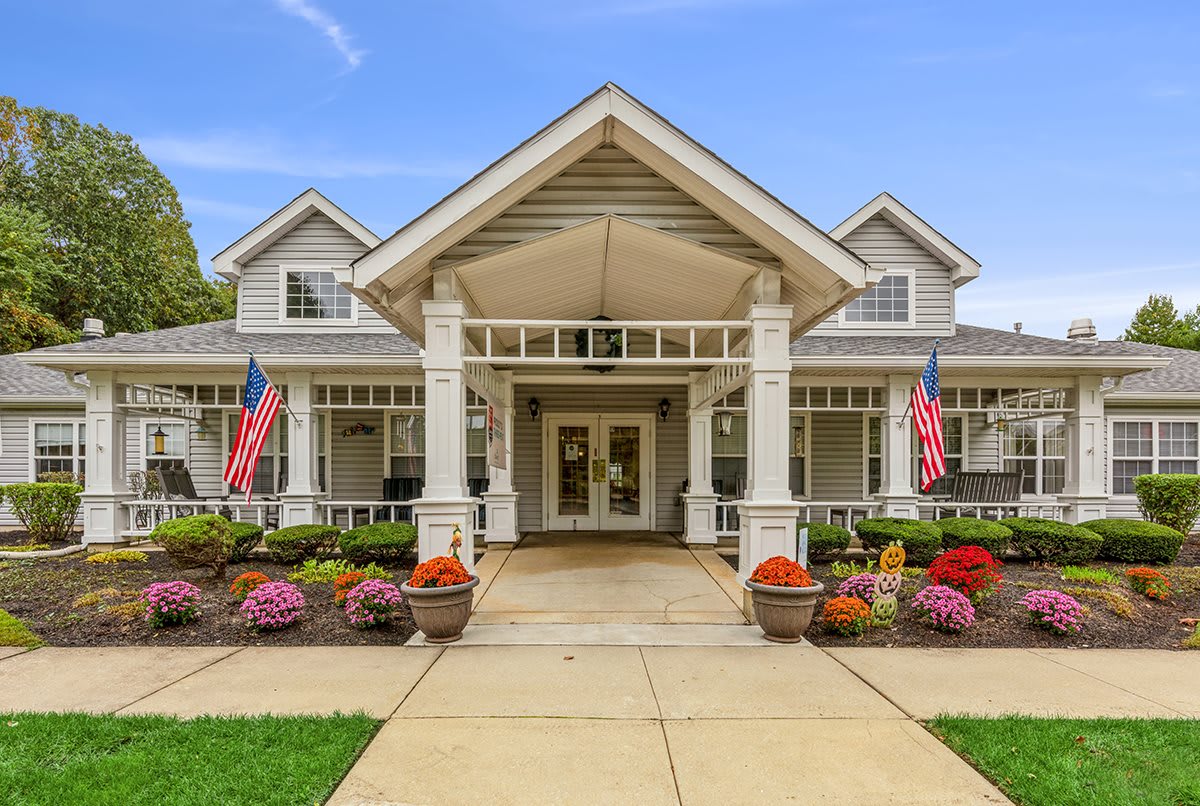 A welcoming entrance of a house with a front porch, decorated with flags and surrounded by landscaped gardens.
