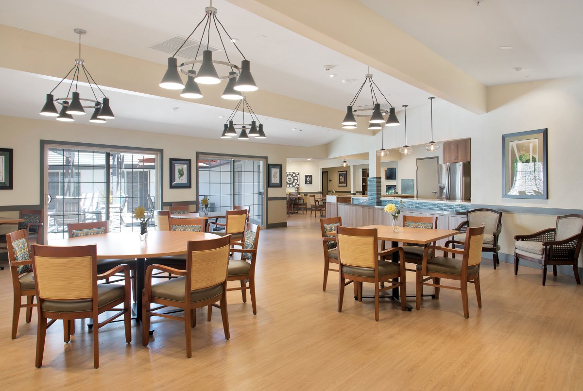 A spacious dining area with modern design elements, featuring multiple tables and chairs under stylish lighting fixtures.