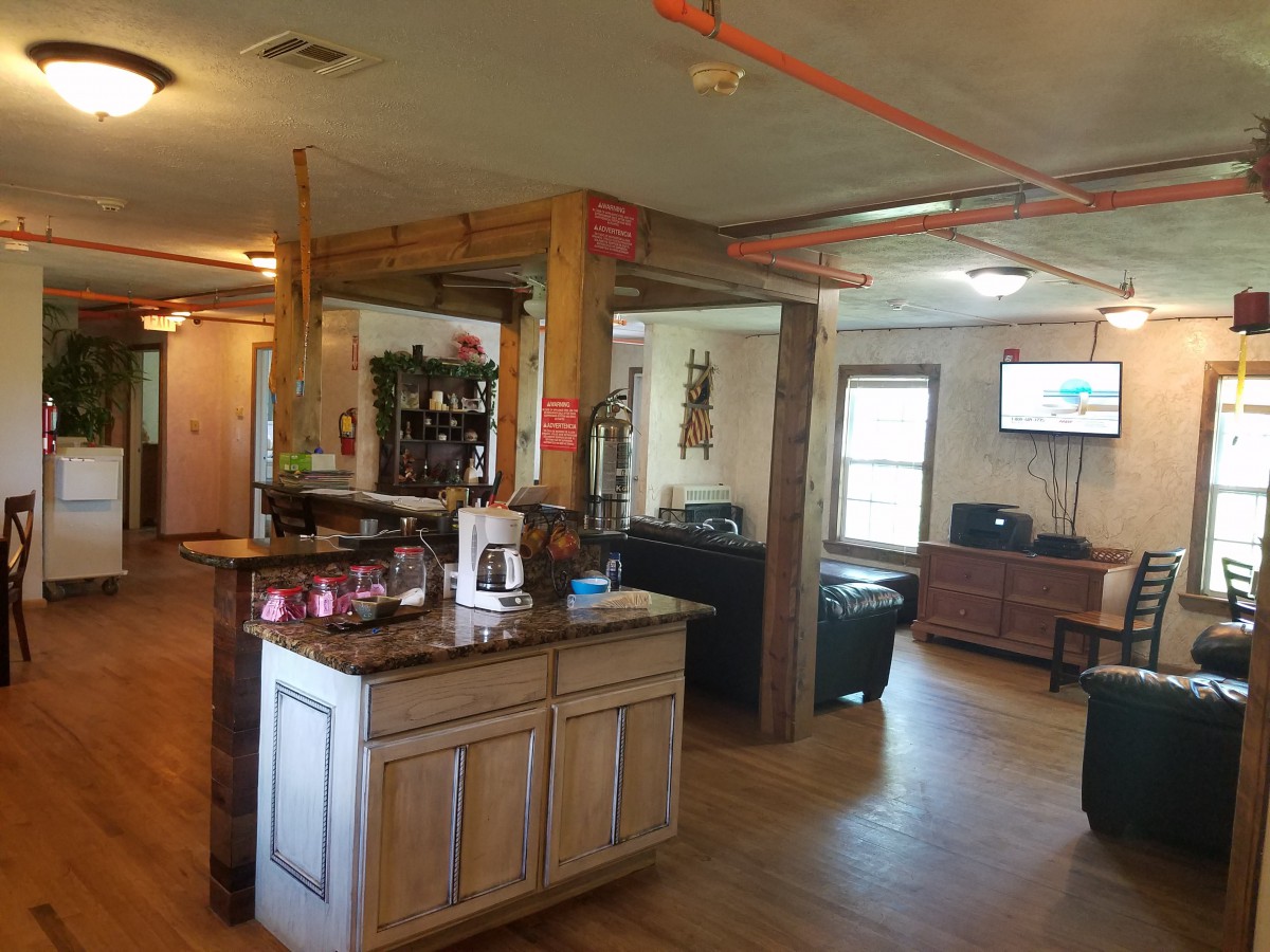 A cozy living space with wooden beams and furniture, showcasing a connected kitchen area and a TV.