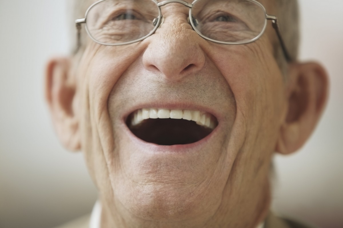 An elderly man wearing glasses joyfully laughing in a close-up shot.