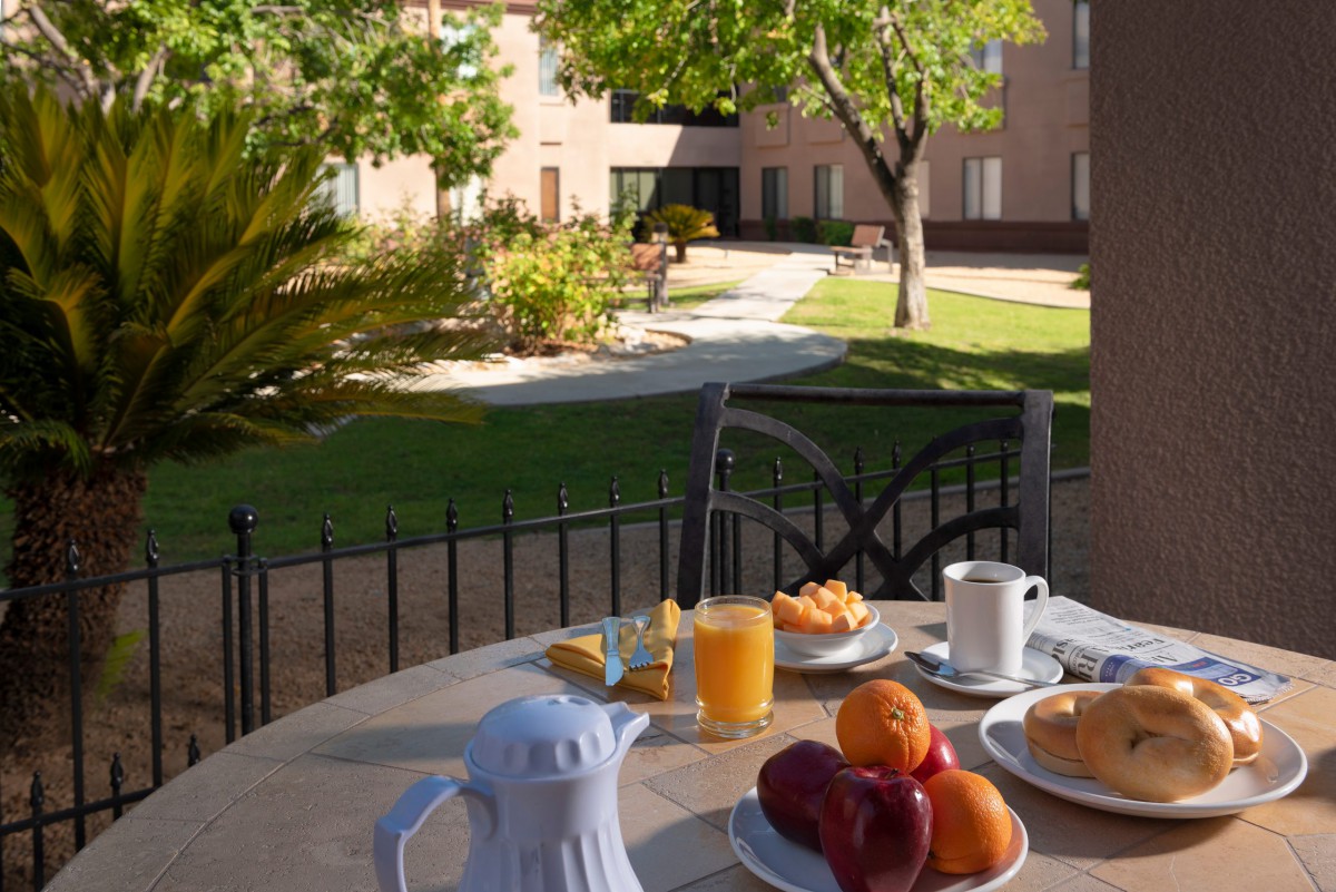A peaceful outdoor breakfast setup on a table in a garden with fruit, orange juice, and coffee.