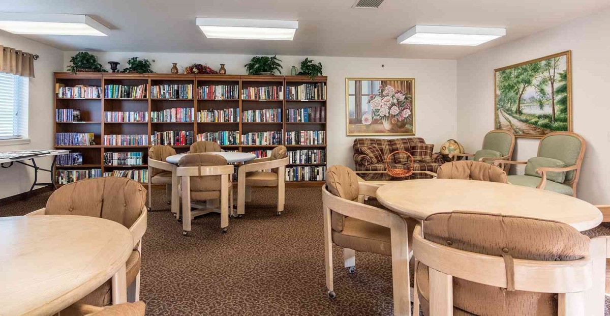 A cozy library space with bookshelves, tables, and chairs for reading.