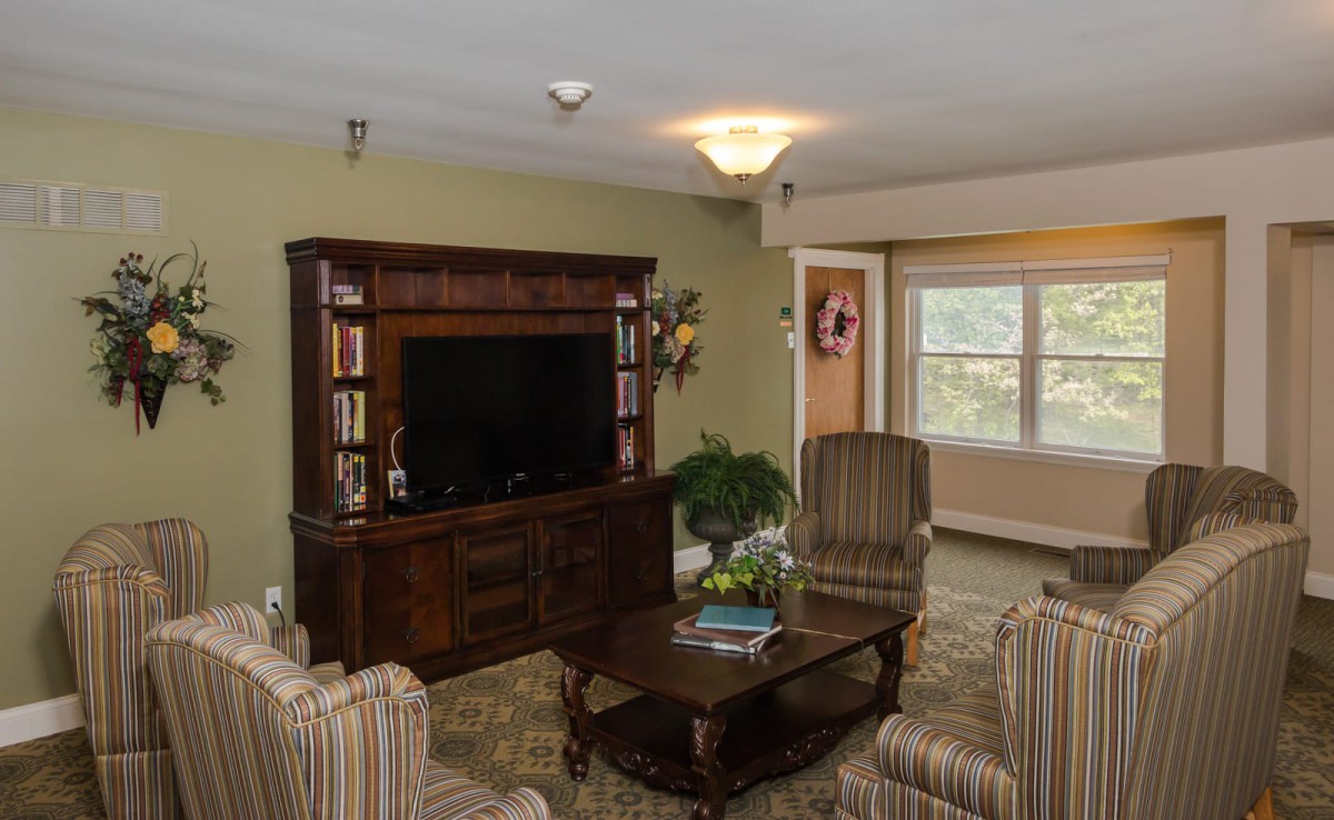 A cozy living room with a television, comfortable chairs, and a bookshelf.