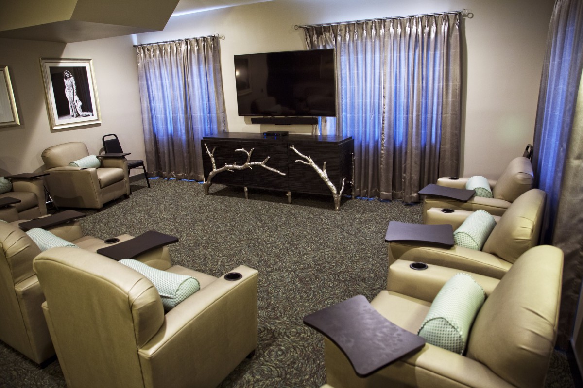 A modern living room with comfortable recliners facing a large television, featuring elegant curtains and contemporary decor.