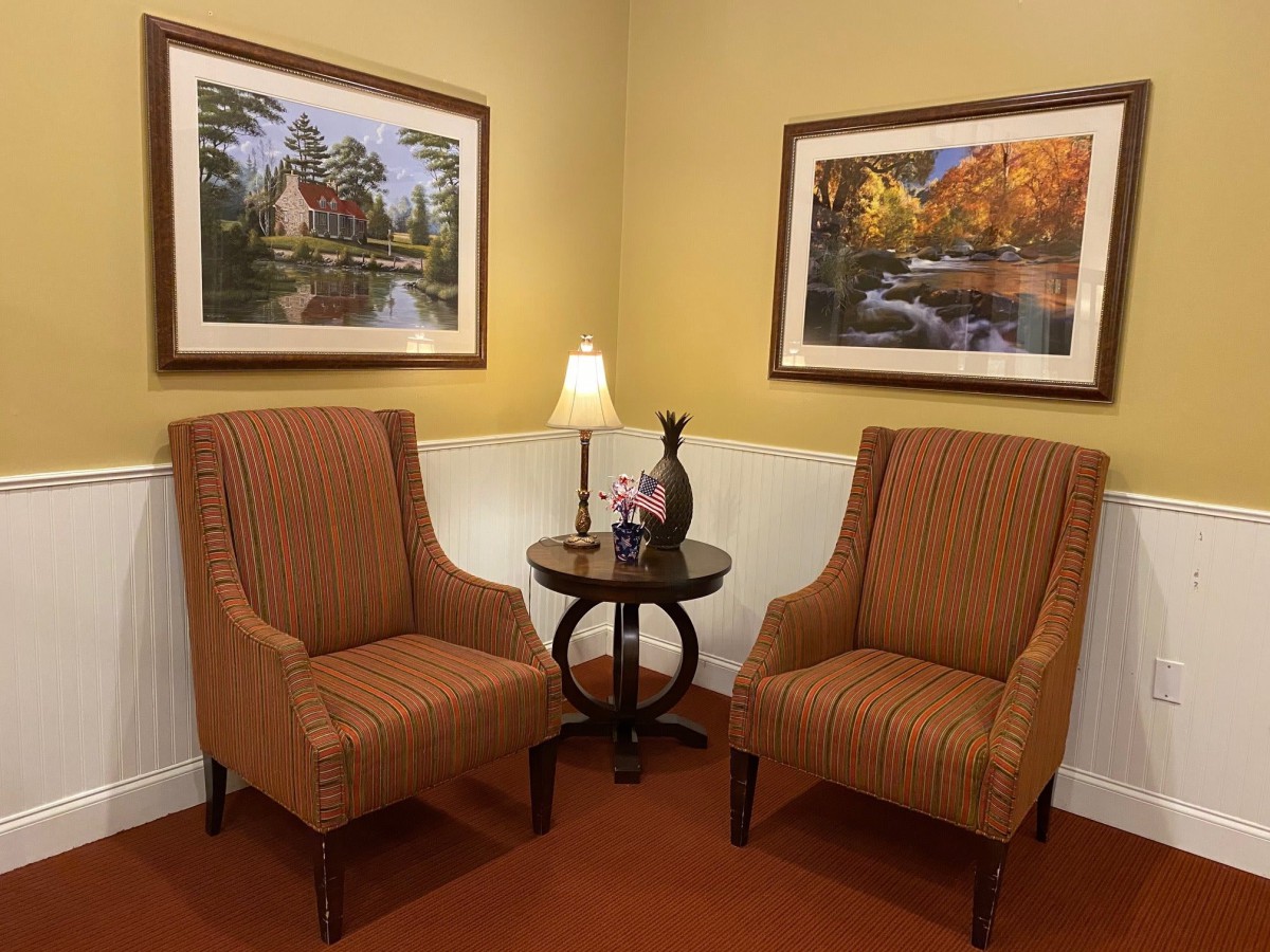 A cozy seating area with two chairs and a small table, adorned with a lamp and flanked by framed paintings.