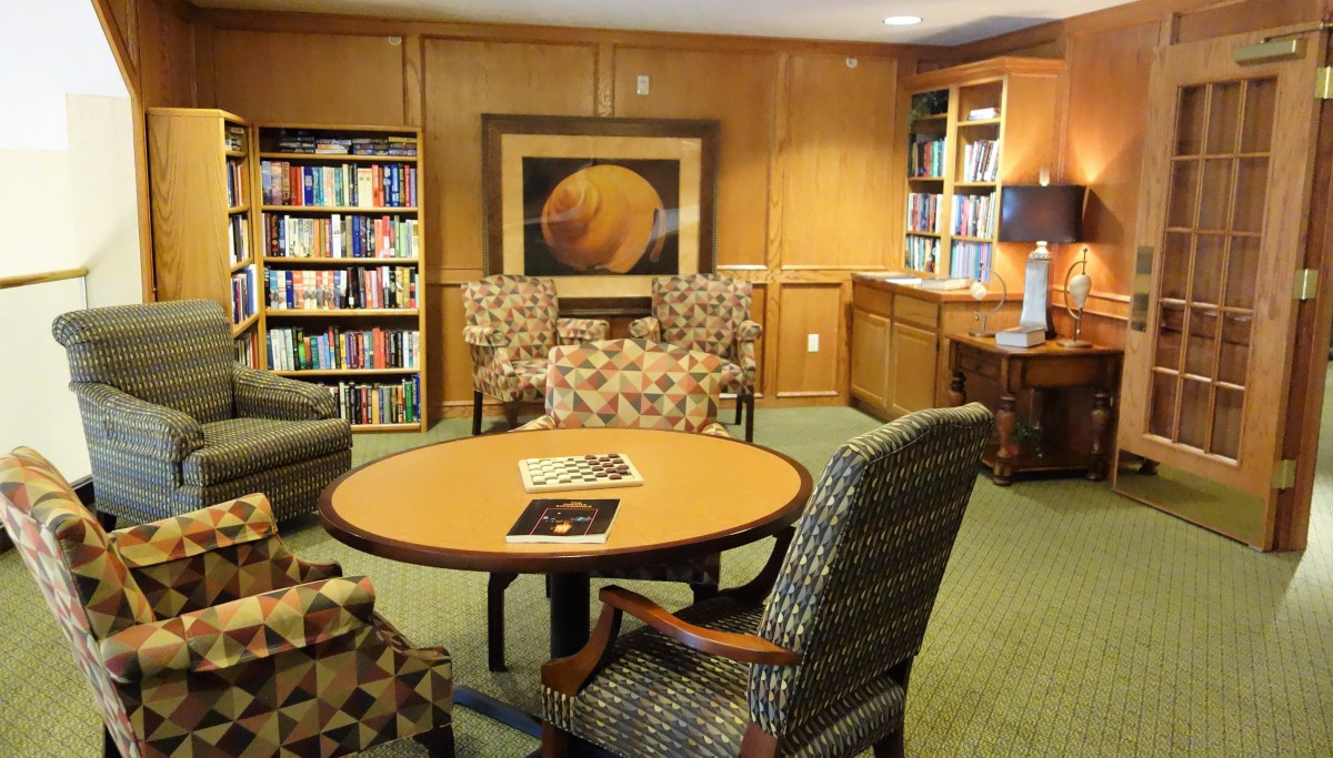 A cozy library reading area with shelves filled with books, a round table, and comfortable chairs.