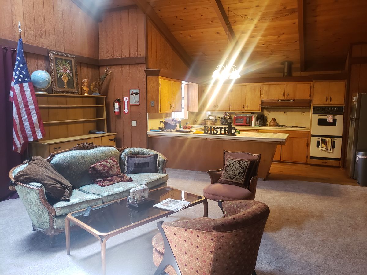 A cozy living room with vintage decor and wood paneling, featuring a comfortable seating area and adjacent kitchen.