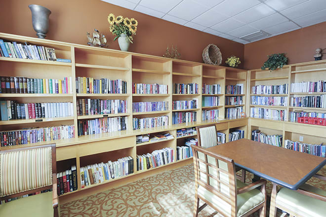 A cozy library reading room with wooden bookshelves filled with books, a table, and chairs.