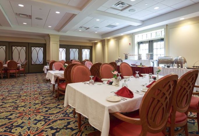 An elegant dining room setup with tables and chairs neatly arranged, adorned with red napkins and place settings.