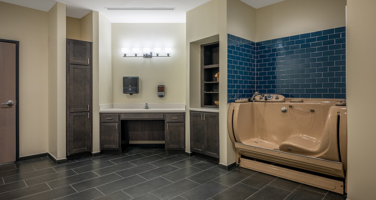 A modern bathroom with a built-in vanity, cabinetry, and a bathtub surrounded by blue tiles.