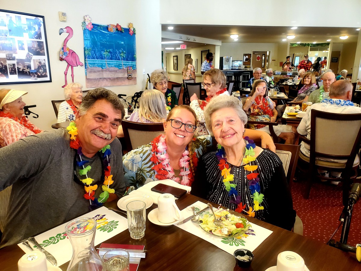 A group of people enjoying a celebration at a dining venue, wearing colorful leis.