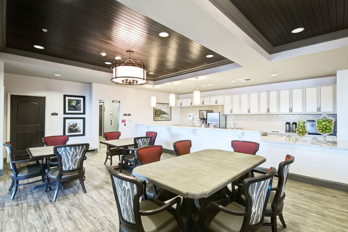 A modern dining area with a well-lit ambiance, featuring stylish chairs and tables, adjacent to a kitchen.