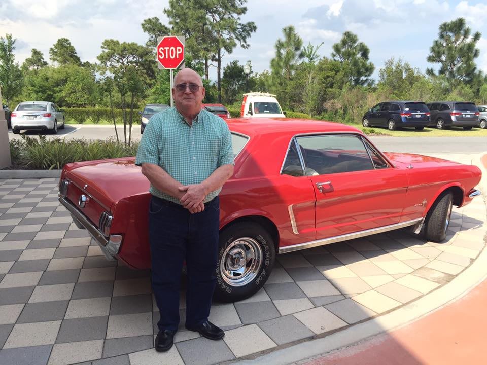 A man standing in front of a classic red Mustang parked outdoors.