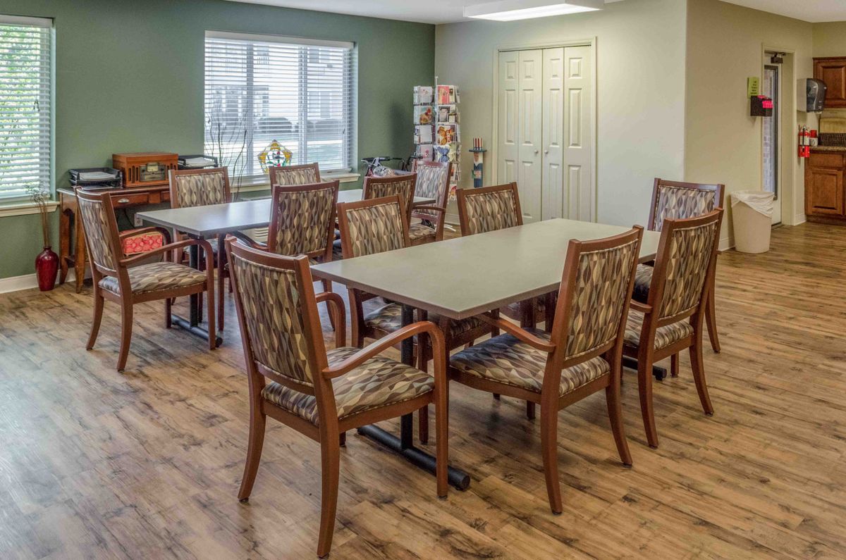 A conference room with wooden tables and cushioned chairs, illuminated by natural light from a large window.
