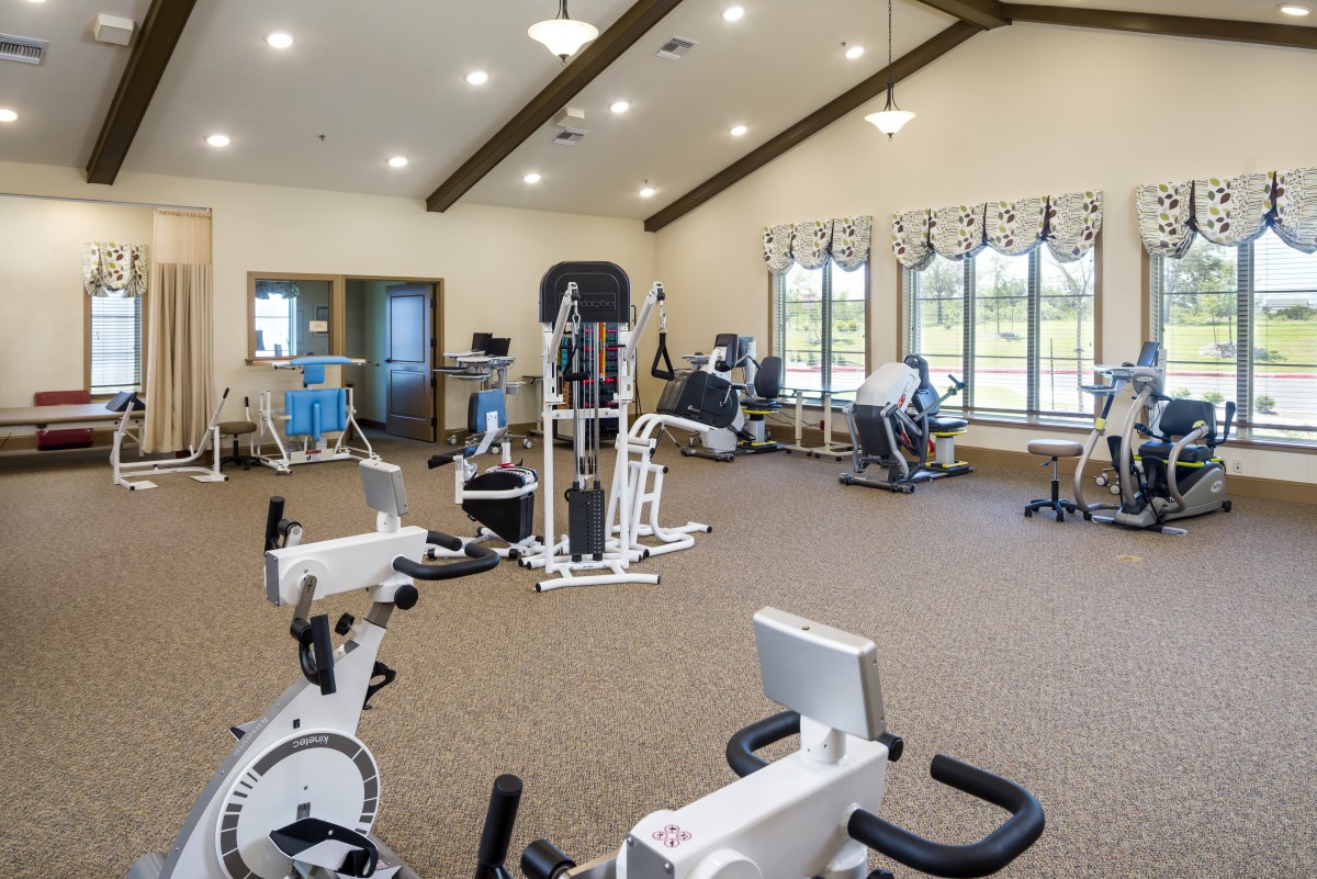 A spacious gym with various exercise equipment and bright natural lighting.