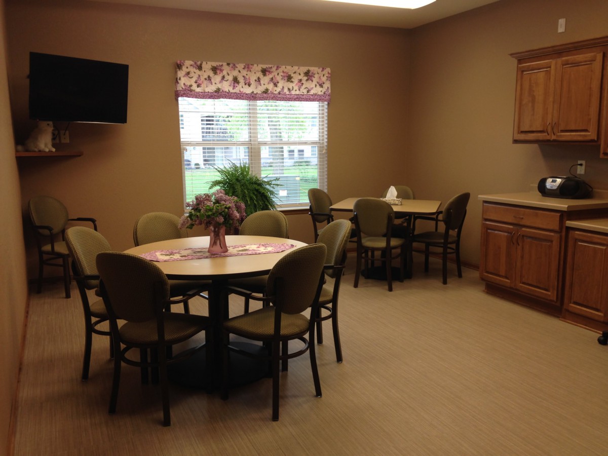 A cozy dining room with multiple tables and chairs, a television on the wall, and a window providing natural light.