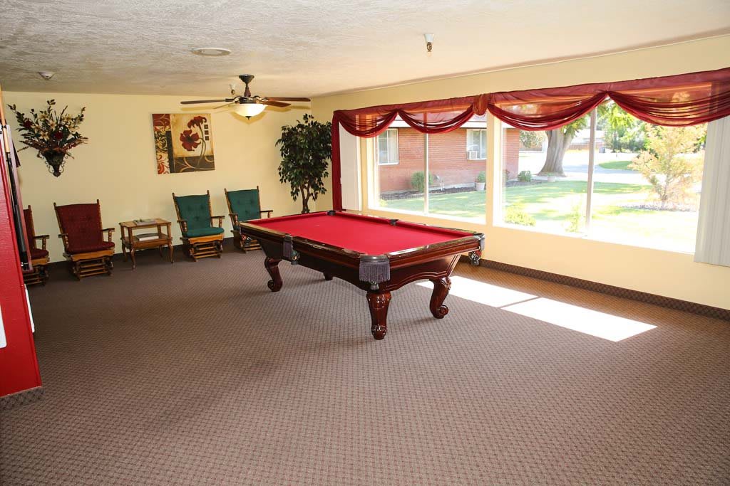 A spacious game room featuring a red pool table with natural light streaming through large windows.