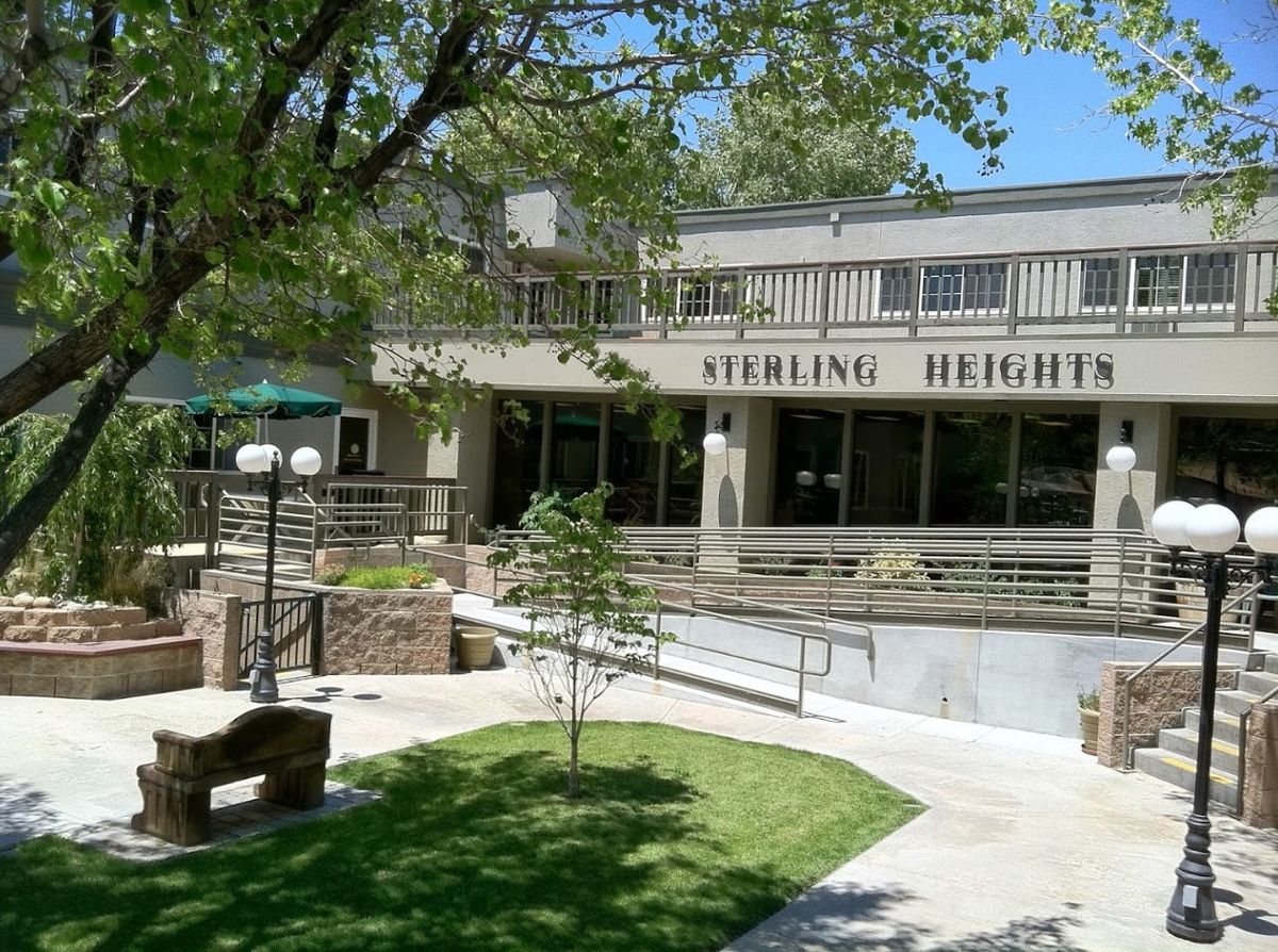Sterling Heights building surrounded by trees and greenery with benches in the foreground.