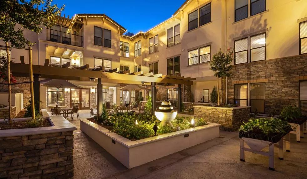 A beautifully lit residential courtyard at night, featuring elegant architecture and lush landscaping.