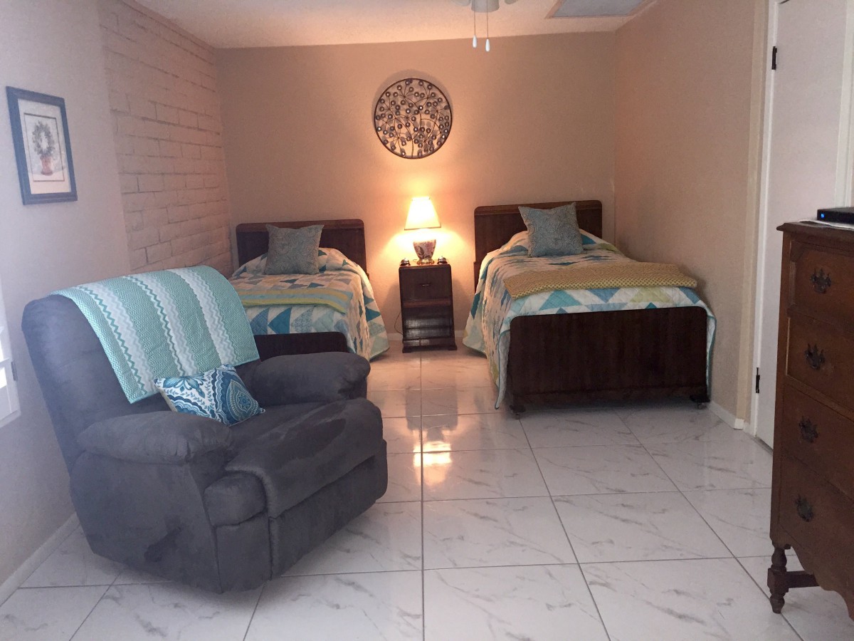 A cozy bedroom with two twin beds, an armchair, and warm lighting.