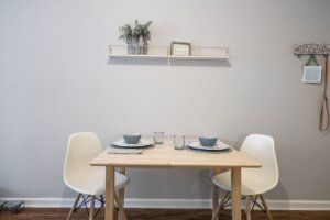 A minimalist dining setup with two chairs and a small wooden table, complemented by a wall shelf with decorations.