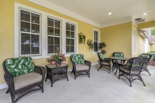A cozy patio area with wicker furniture and potted plants against a yellow wall.