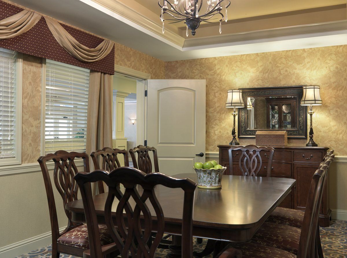 Elegant dining room with a large wooden table and chairs, featuring a chandelier and decorative curtains.