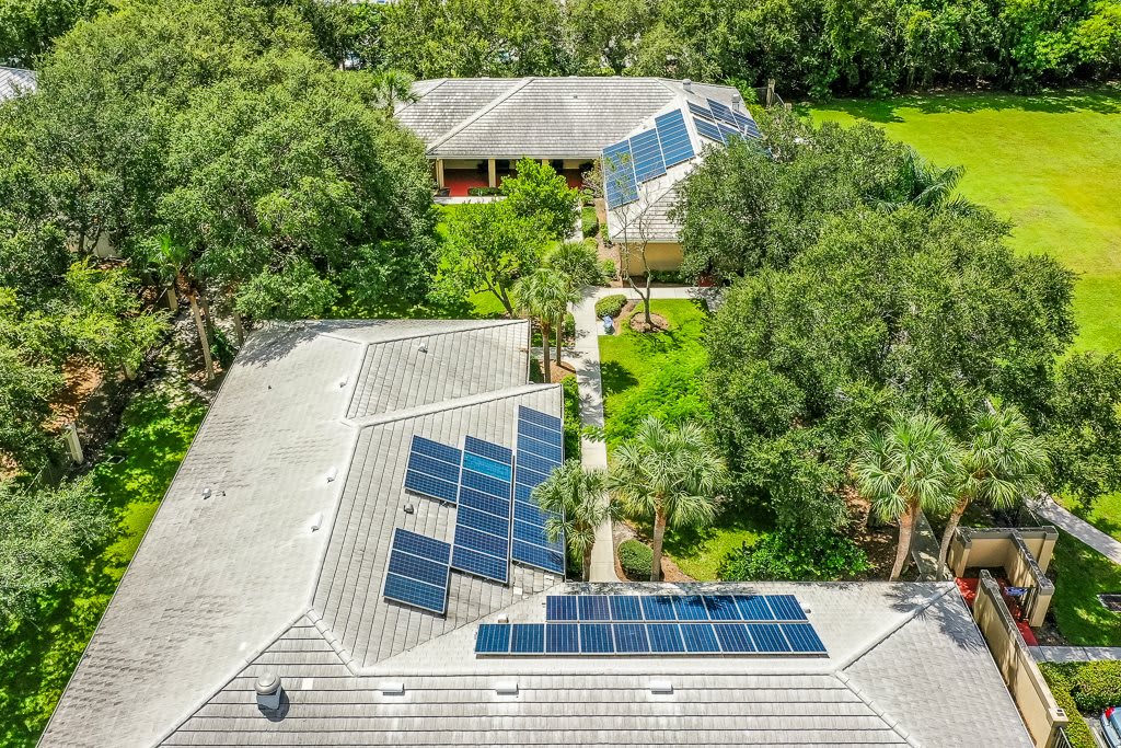 Aerial view of houses with solar panels surrounded by lush greenery.
