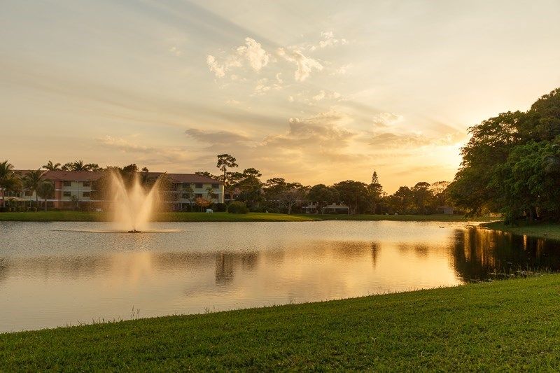A tranquil sunset over a lake with a fountain and surrounding landscape.