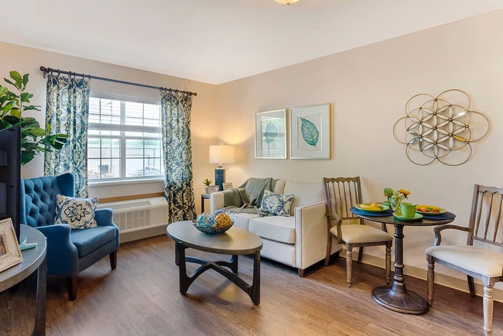 A cozy living room with modern decor, featuring a sofa, coffee table, and natural light from a large window with curtains.