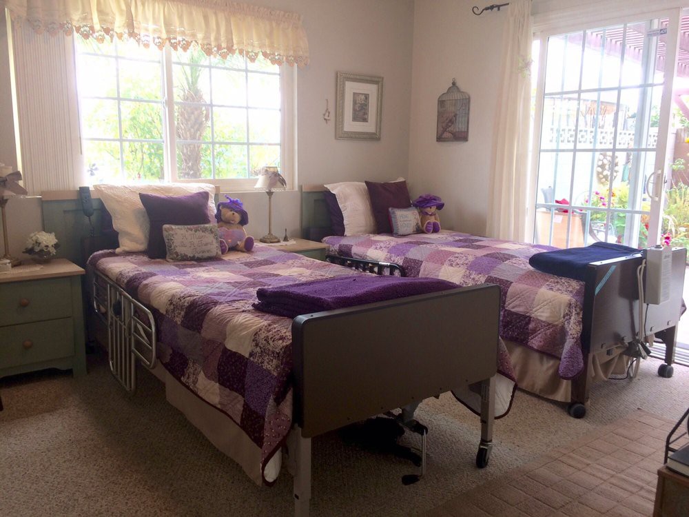 A cozy bedroom featuring twin beds with patchwork quilts and decorative pillows, well-lit by large windows.